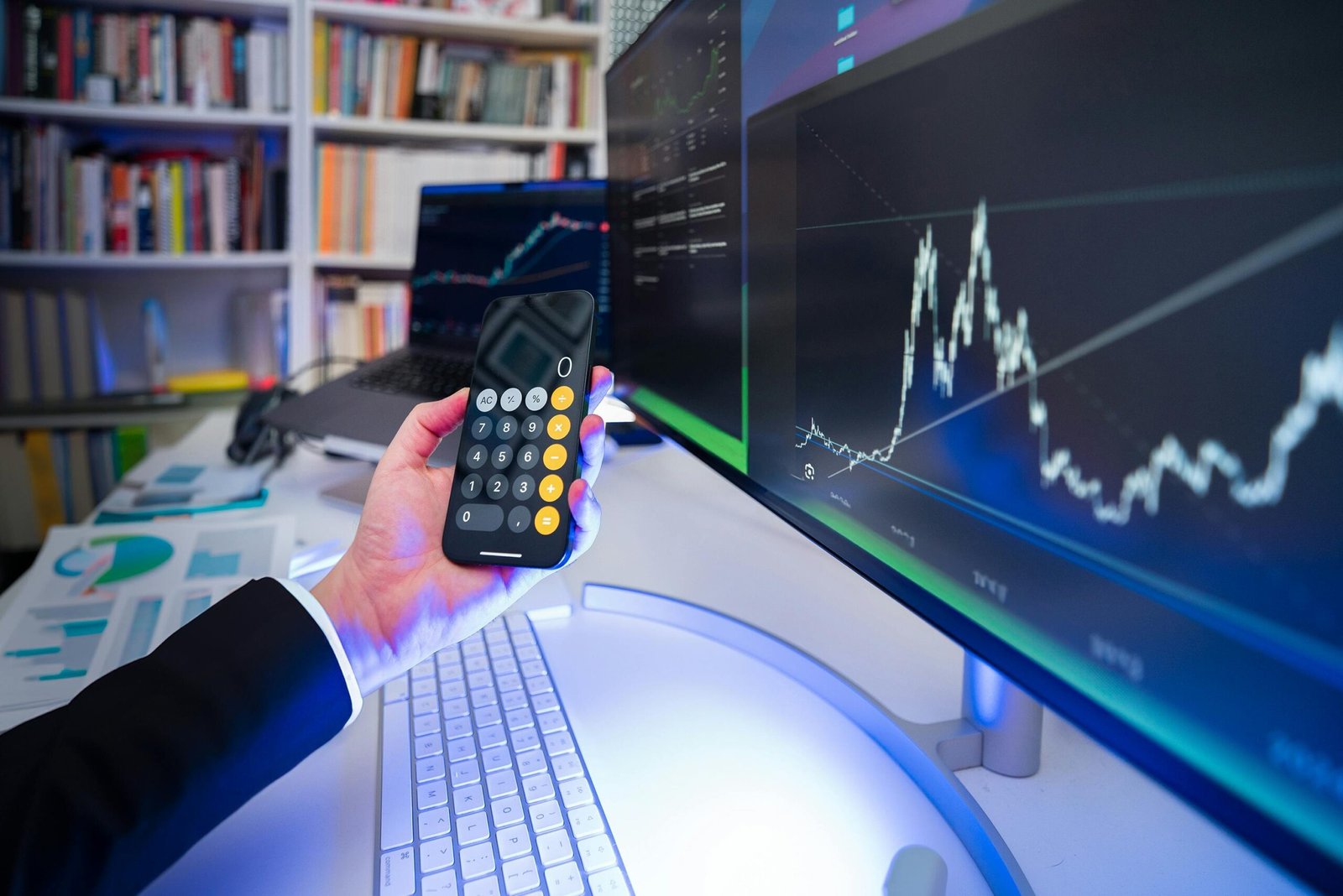 Child holding a calculator while looking at a laptop screen displaying budget charts